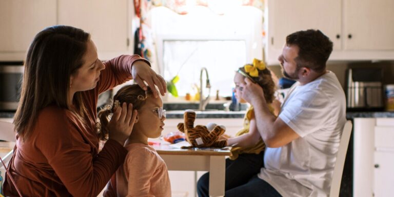 Mother And Father Doing Their Twins Hair Together At Kitchen Table