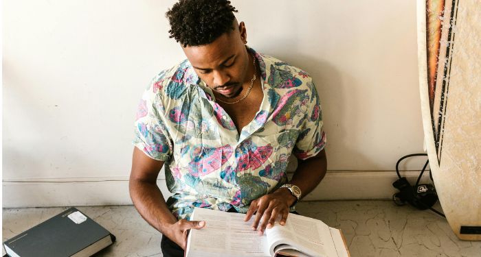 brown skinned black man sitting on floor and reading books surround him.jpg.optimal