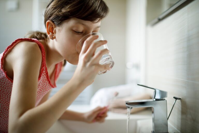 girl drinking water holding toothbrush