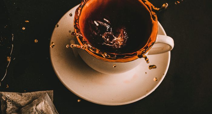 tea spilling out of a tea cup on a saucer against black background.jpg.optimal